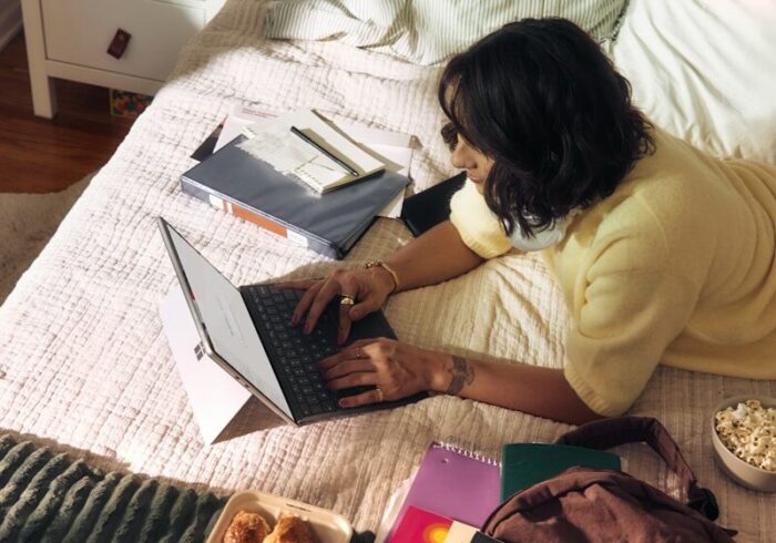 Woman working on laptop on bed with snacks and books.